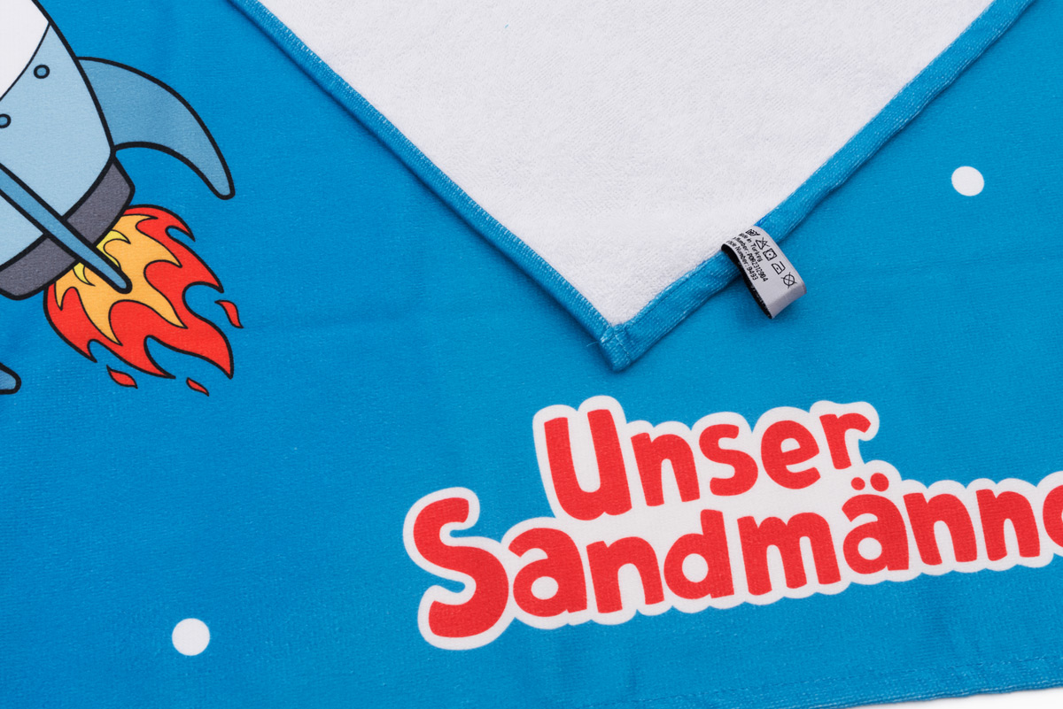 sandmaennchen-im-all-badetuch-badehandtuch-detail-logo Unser Sandmännchen im Weltall Badetuch